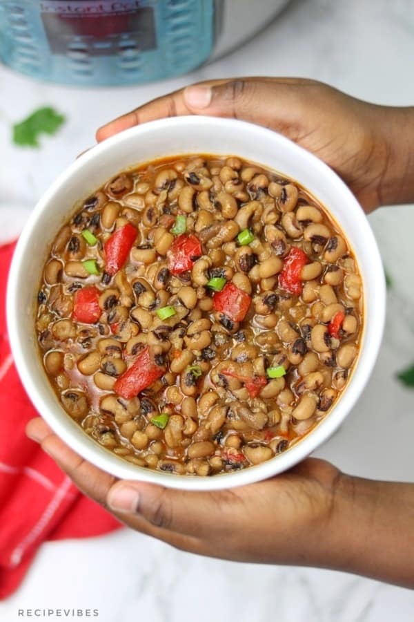 hands holding up a plate of instant pot black eyed peas