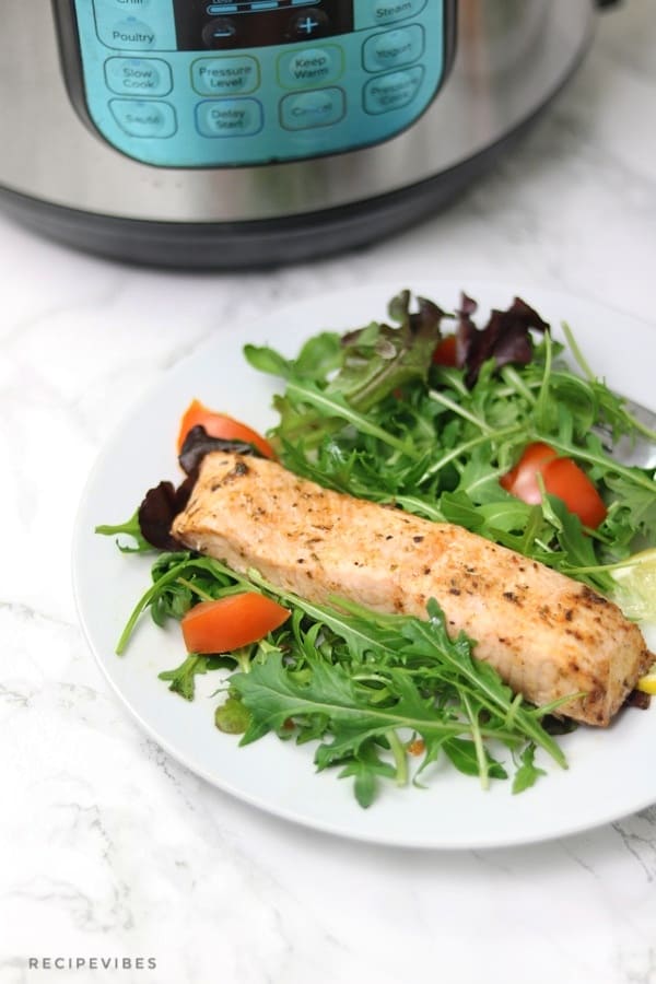 Plate of salmon on salad placed in front of instant pot pressure cooker