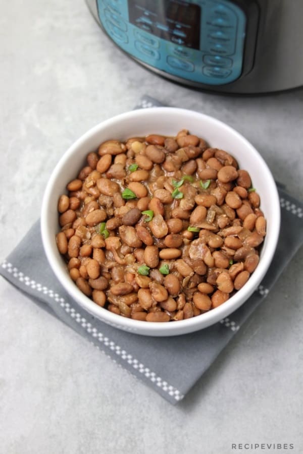 Instant pot pinto beans in white plate garnished with spring onions and placed on napkin