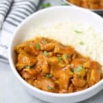 butter chicken with rice in a white plate garnished with coriander