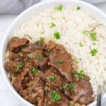 beef tips served on white rice in a plate.
