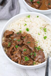 beef tips served on white rice in a plate.
