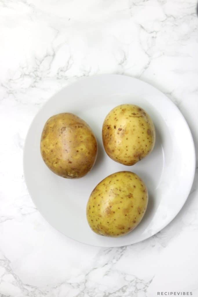 Scrubed and washed baking potatoes on white flat plate