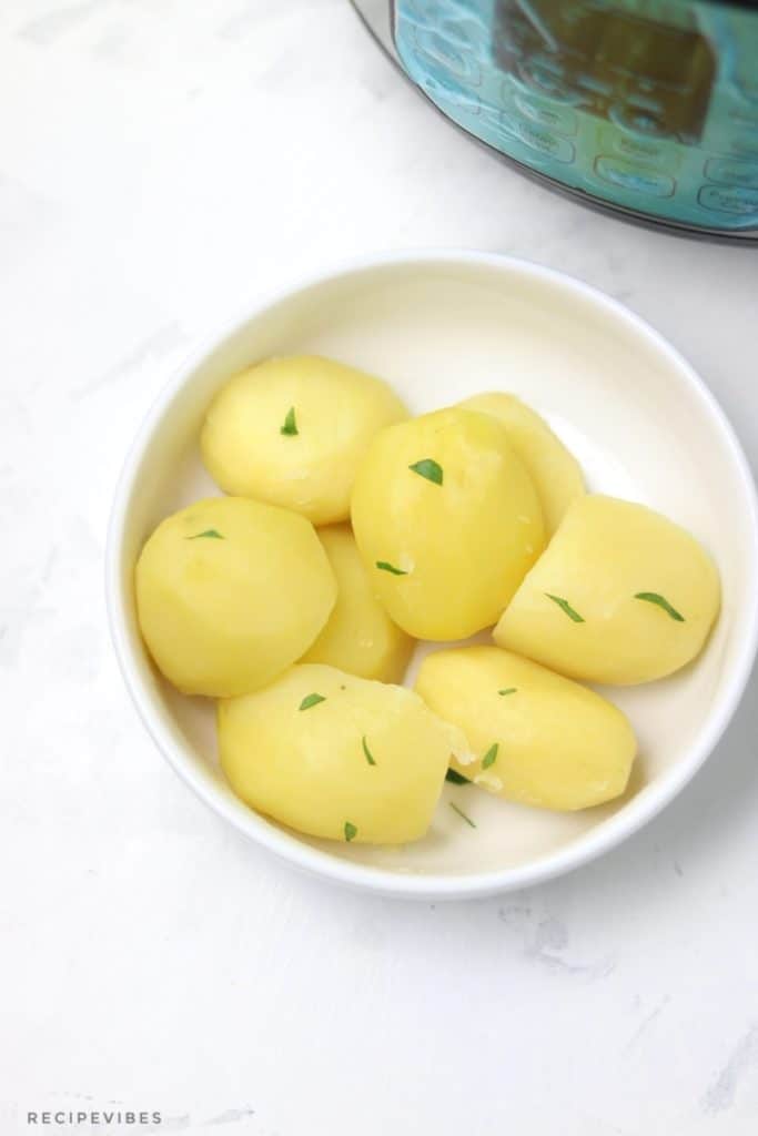 boiled potatoes in white plate displayed in front of instant pot