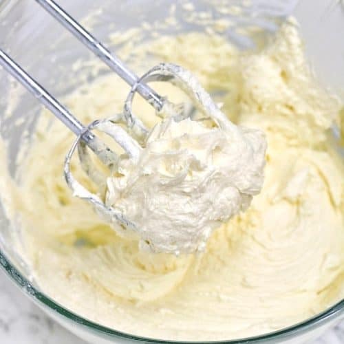 buttercream icing inside a mixing bowl and on hand mixer blades.