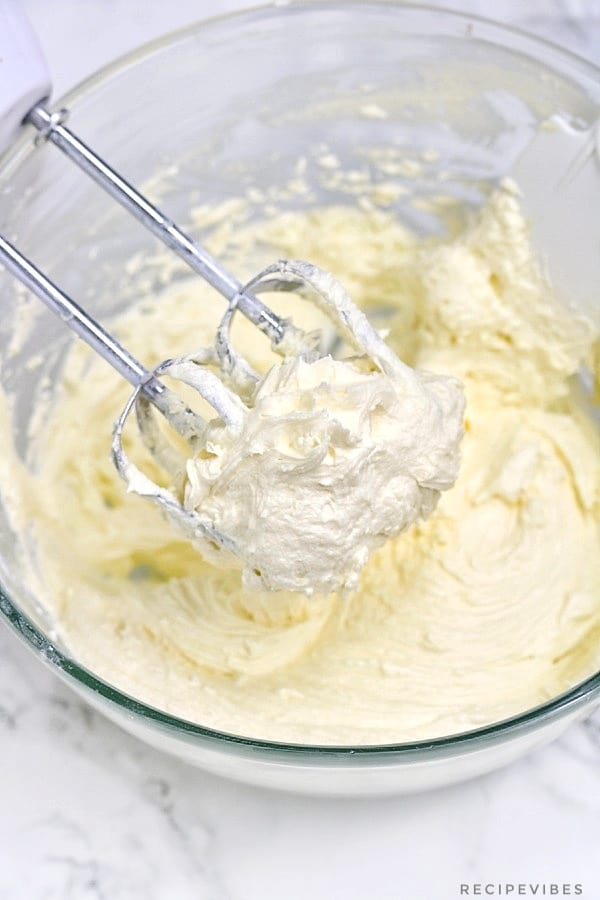 buttercream icing inside a mixing bowl and on hand mixer blades.