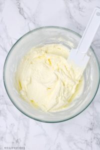 fluffy buttercream frosting in a glass bowl with white spatula inserted in the bowl.