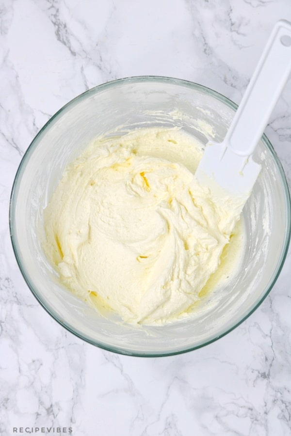 fluffy buttercream frosting in a glass bowl with white spatula inserted in the bowl.