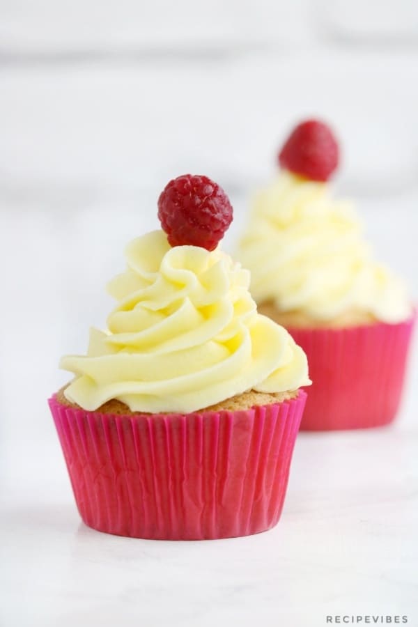 2 cupcakes with buttercream piped on them and raspberry placed on the frosting on each of them.
