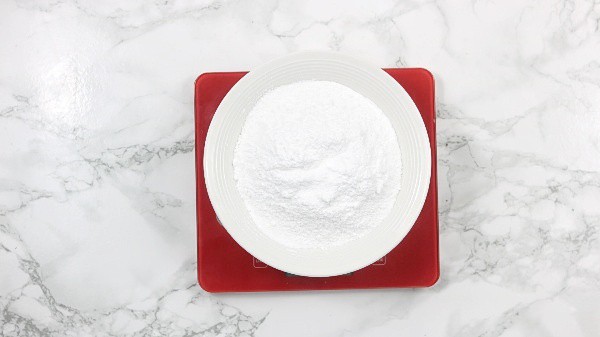 icing sugar in a bowl placed on a red digital kitchen scale.