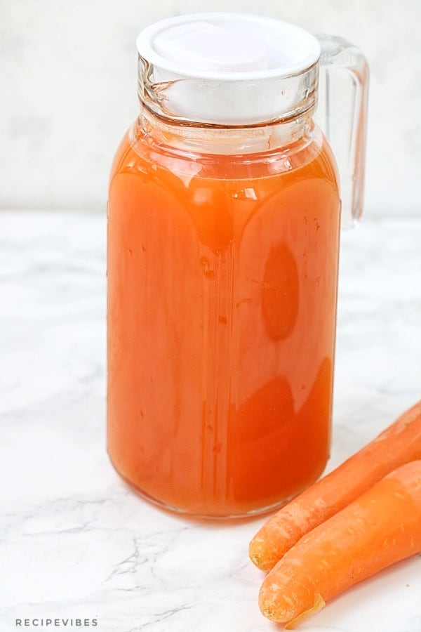 carrot juice in a glass pitcher wth raw carrots on the side