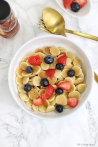 cereal pancakes topped with strawberries and blueberries in a white bowl