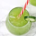 cucumber juice in a cup garnished with a cucumber slice with red and white stripe straw inserted.