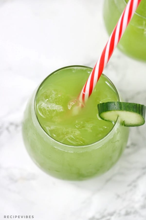 cucumber juice in a cup garnished with a cucumber slice with red and white stripe straw inserted.
