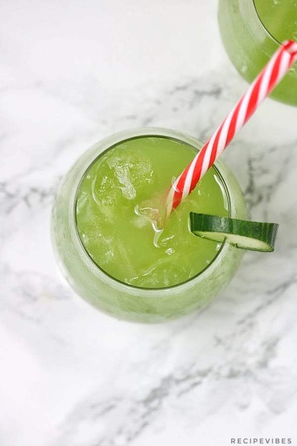 cucumber juice in a glass cup with cucumber slice garnish and a red and white stripe straw inserted.