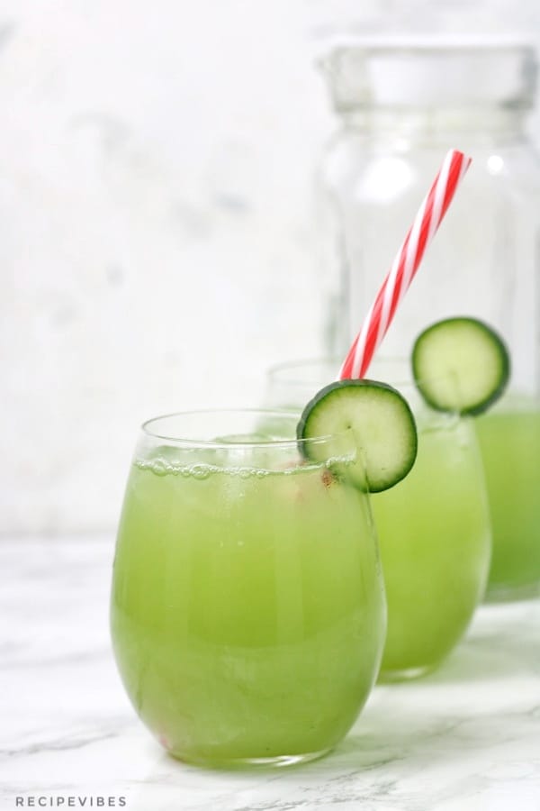 lime juice in a pitcher and two glass cups. The glass cups are garnished with cucumber slices and straw inserted in one of the cups.