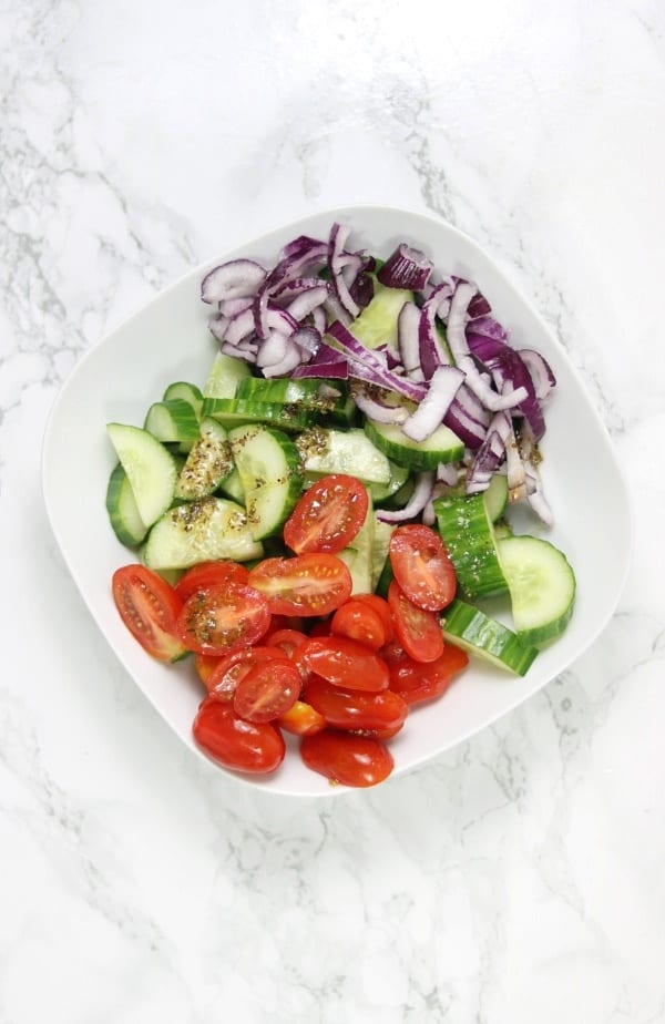 cucumber, tomatoes, onions and salad dressing in a bowl