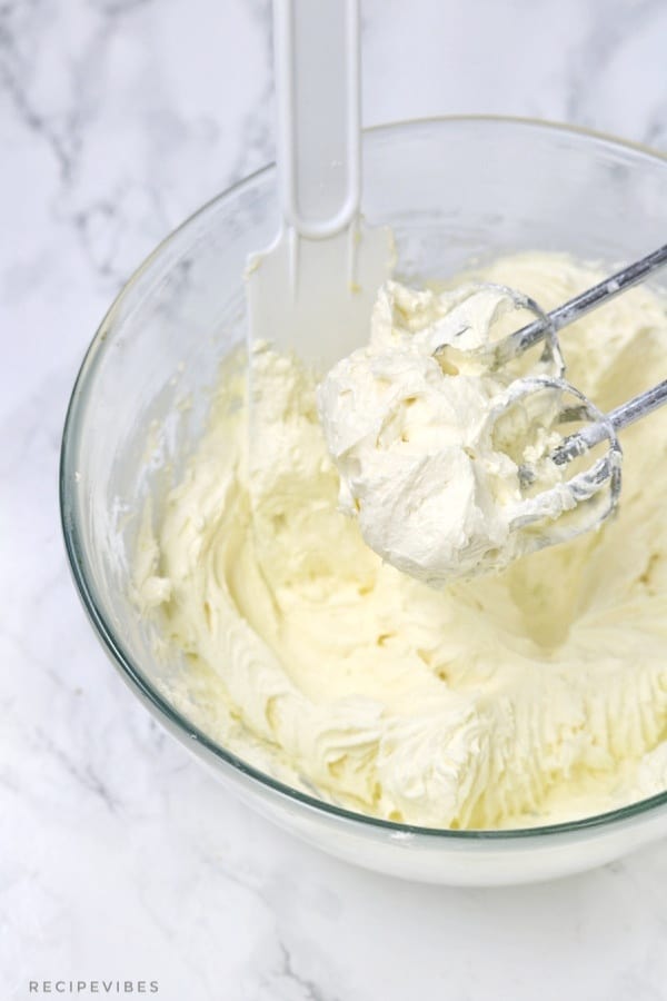 buttercream in a mixing bowl with spatula and handmixer blades inside the bowl.