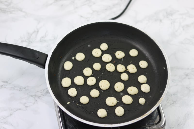 pancake batter piped  in tiny sizes inside nonstick pan.