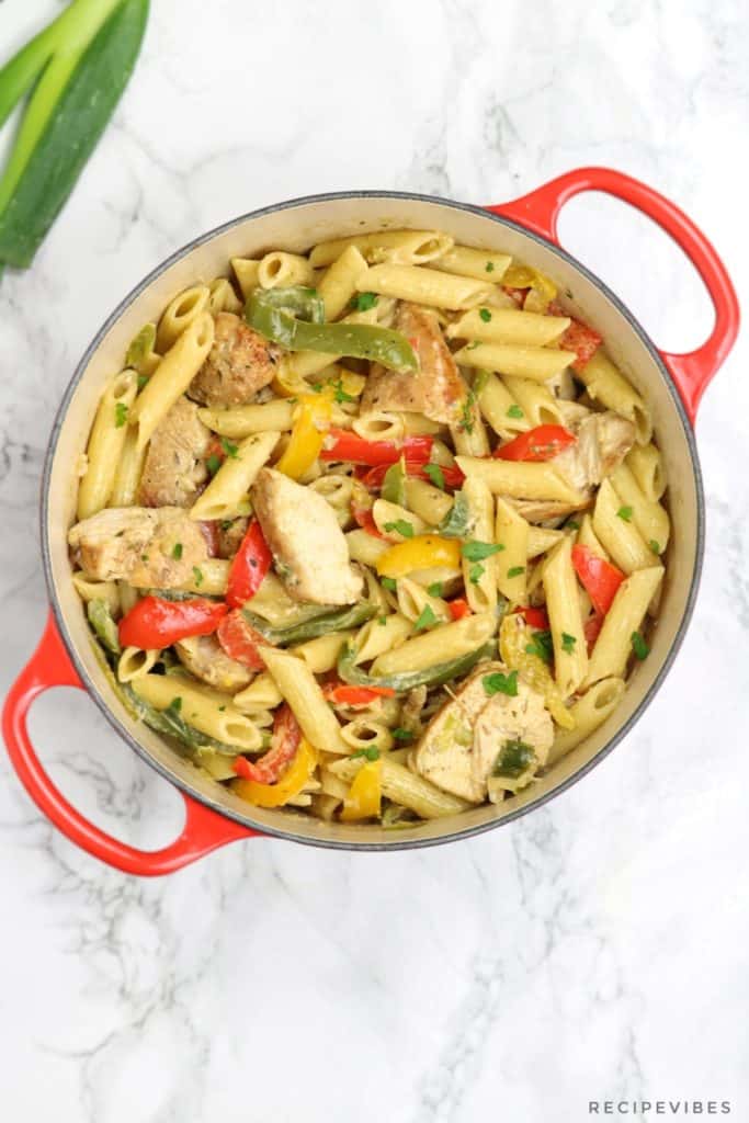 Jerk chicken rasta pasta in a red placed on a white surface.