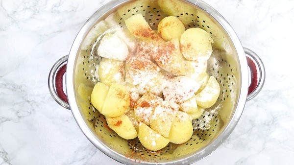 flour and paprika added to the potatoes in a colander
