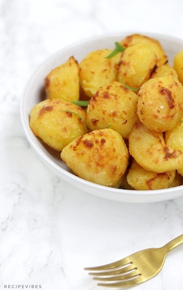Roast potatoes in a white bowl with gold fork in view