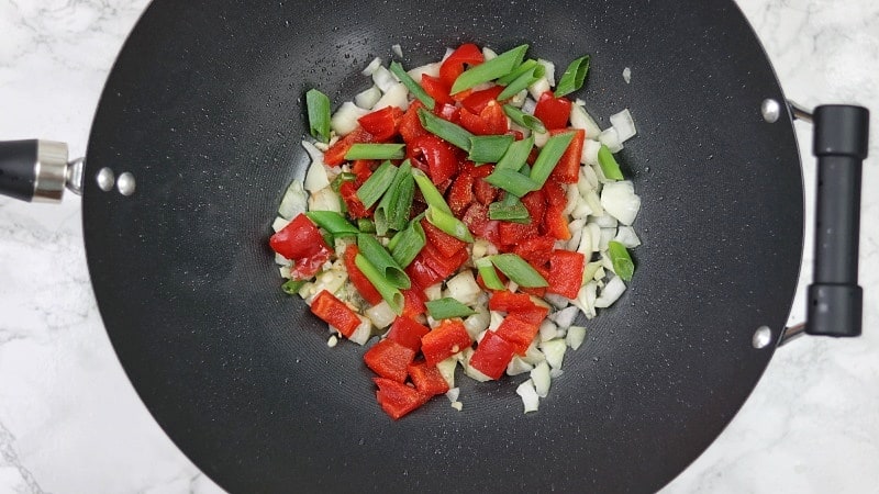 onions, garlic, scallions, chillies and bell peppers in a black wok.