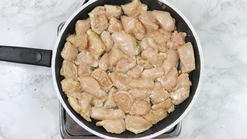 marinated chicken pices being fried in a frying pan.