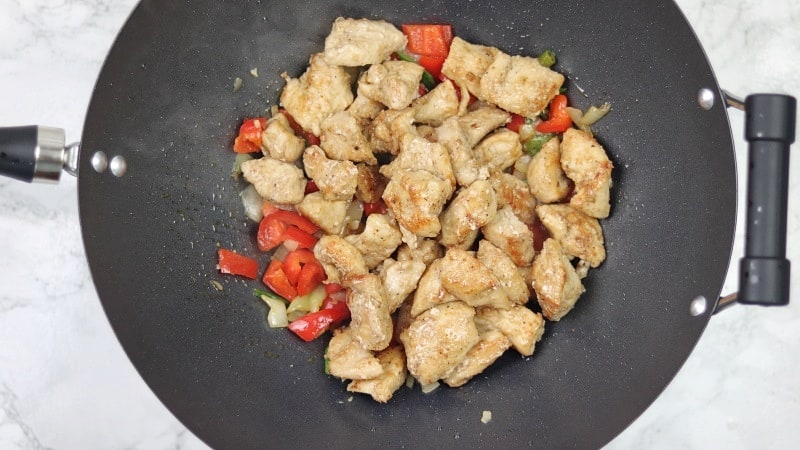 fried chicken pieces added into the wok with onions, chillies and peppers.