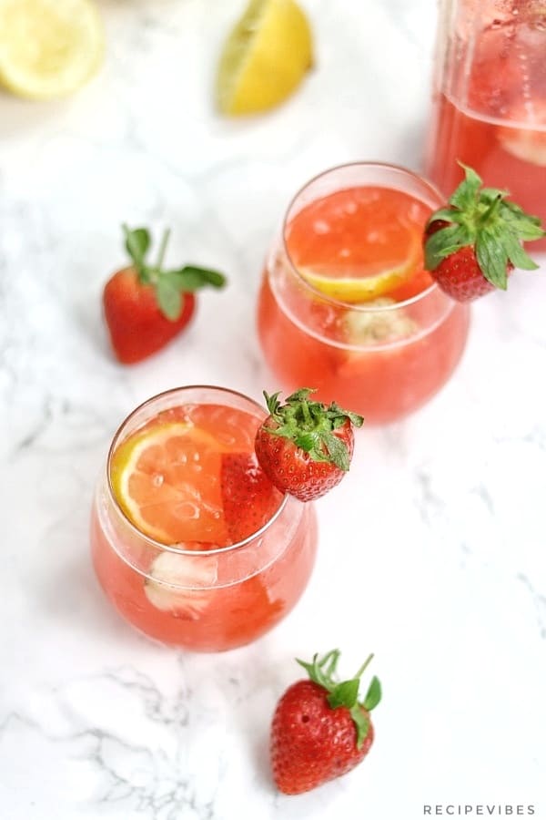 strawberry lemonade in pitcher and 2 glass cups garnished with fresh strawberries