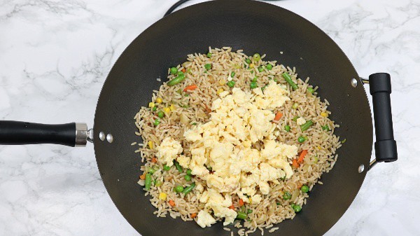 scrambled eggs on top of the rice and vegetables in a wok.