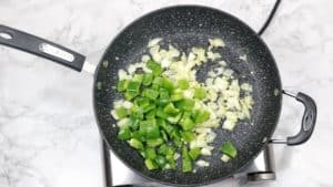 onions, garlic and green chopped bell peppers inside a skillet.