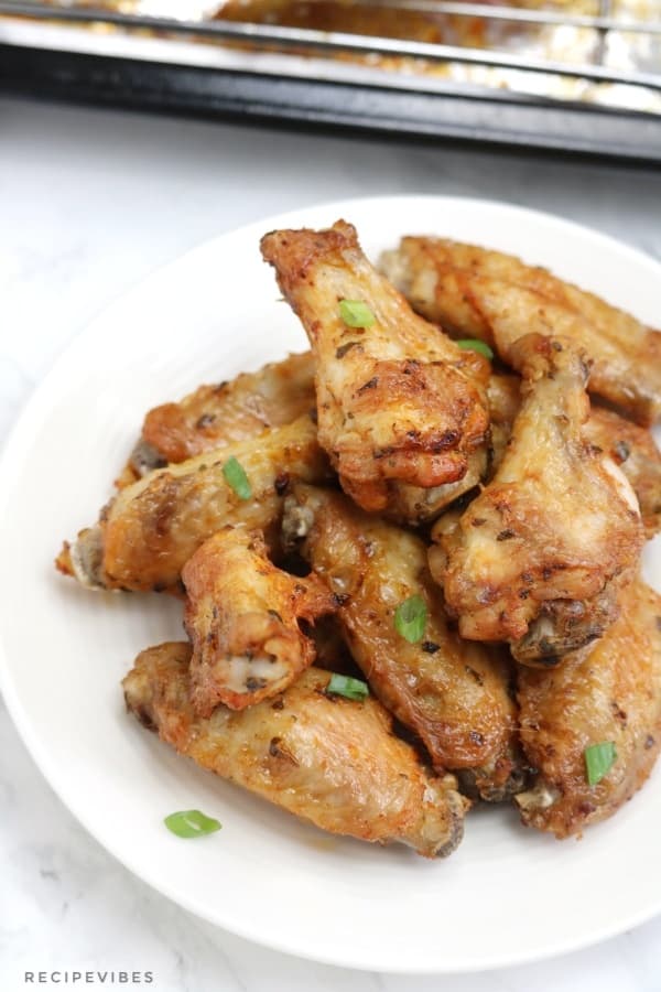 baked chicken wings piled on a plate and garnished with spring onions.