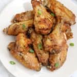 chicken wings on a white plate and garnished with green onions.
