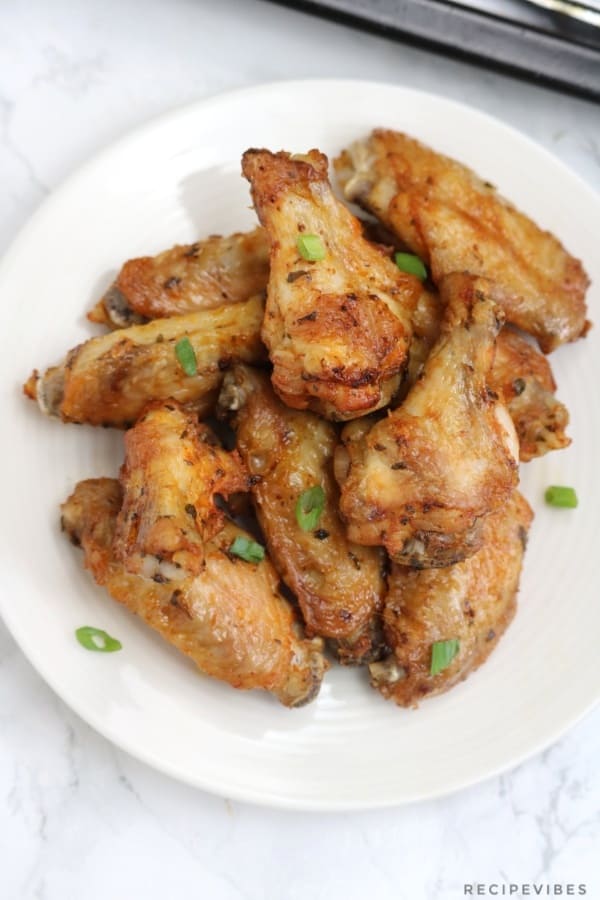 chicken wings on a white plate and garnished with green onions.