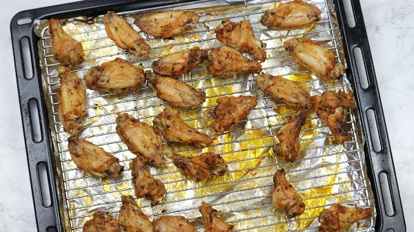 Crispy baked chicken wings on rack on oven tray.