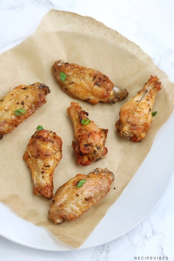 Baked chicken wings on parchment paper line plate.
