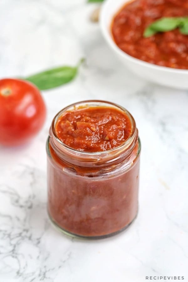 marinara sauce in a jar with a tomato and basil leave in the background.