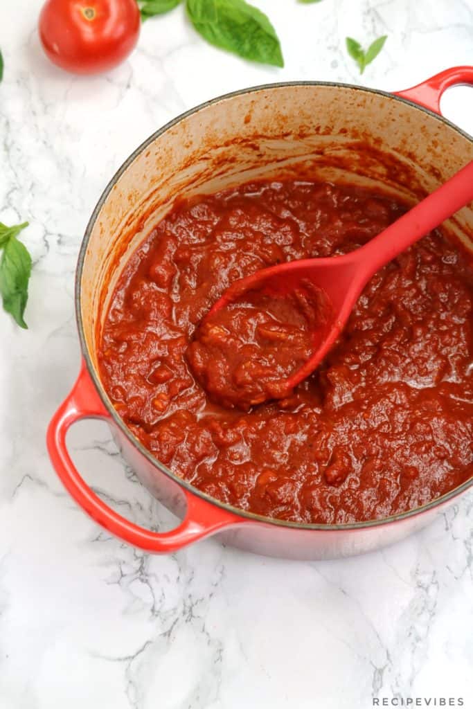 The  sauce in a red pot with red cooking spoon inserted in the pot.