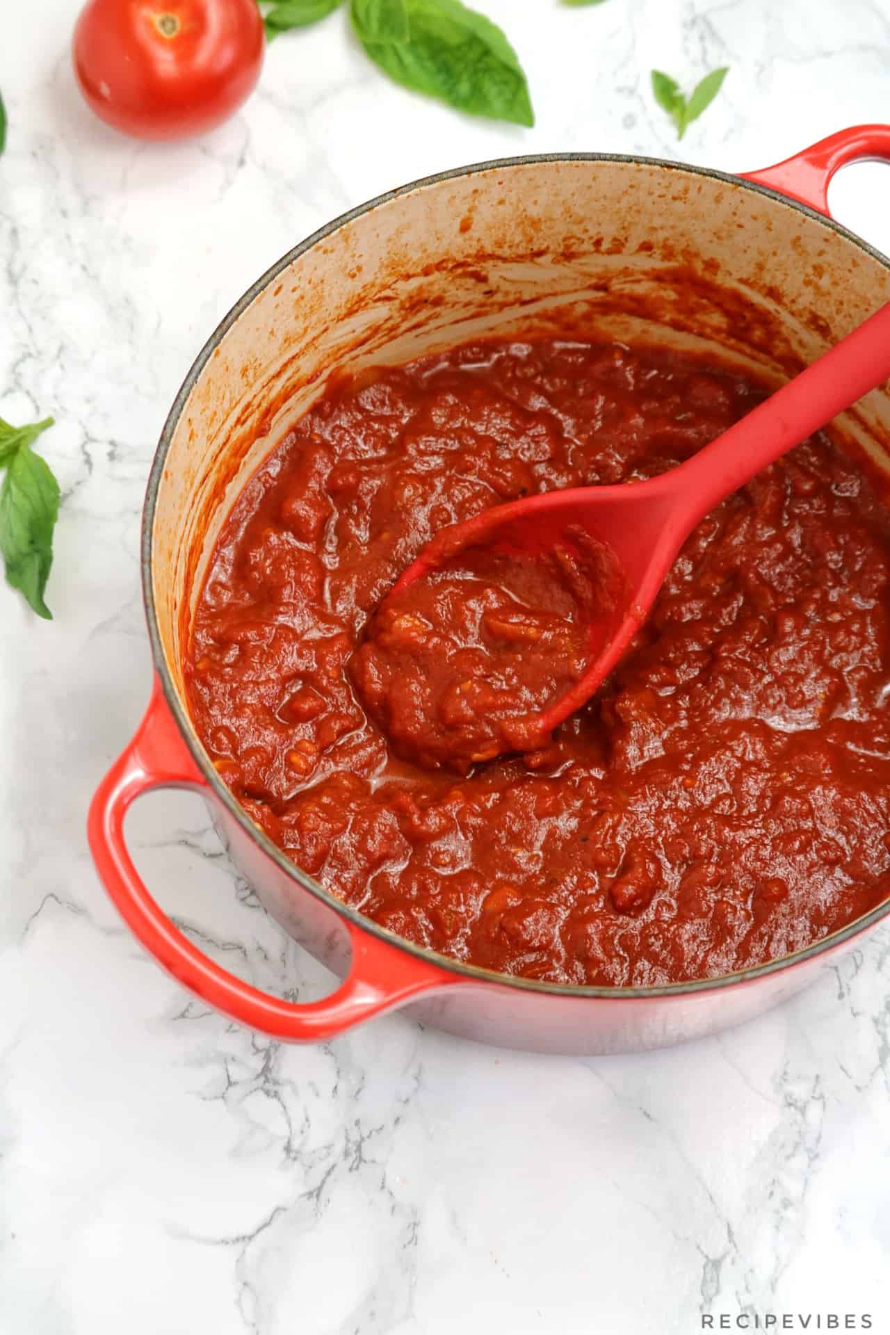 marinara sauce in a red pot with red cooking spoon inserted in the pot.