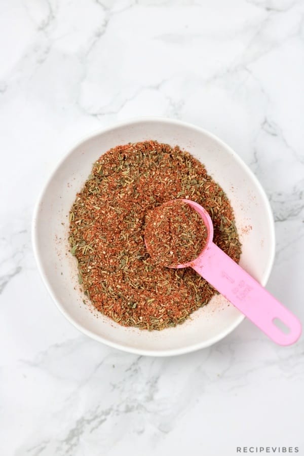 Mixed chicken spice rub in a cream bowl with pink spoon inserted.