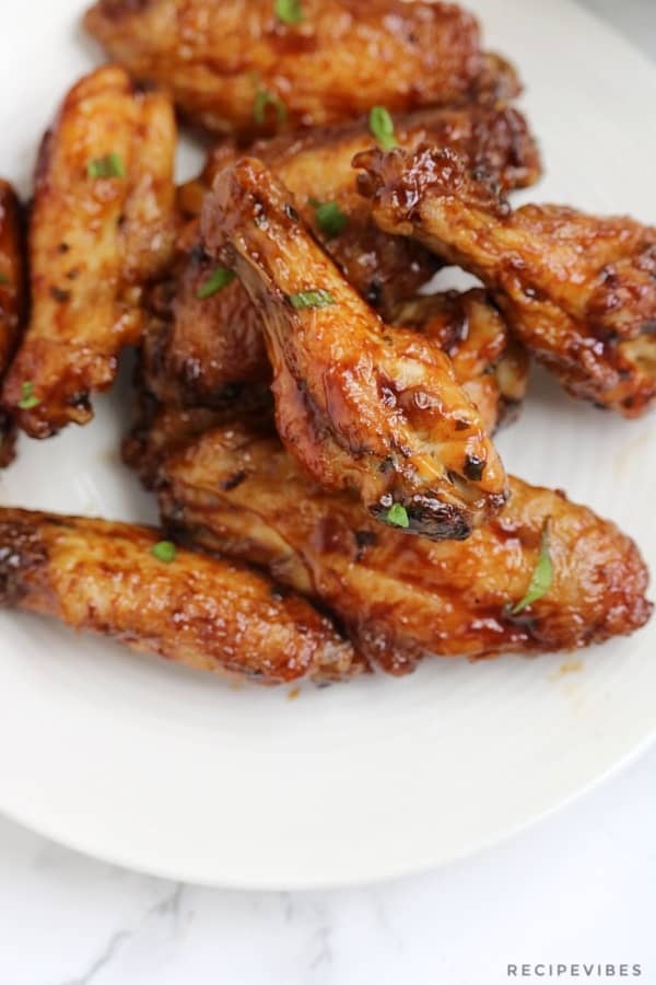 Honey soy chicken wings served on a cream plate and garnished with chopped green onions.