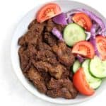 Suya served with onion,tomatoes and cucumber slices in light blue plate.