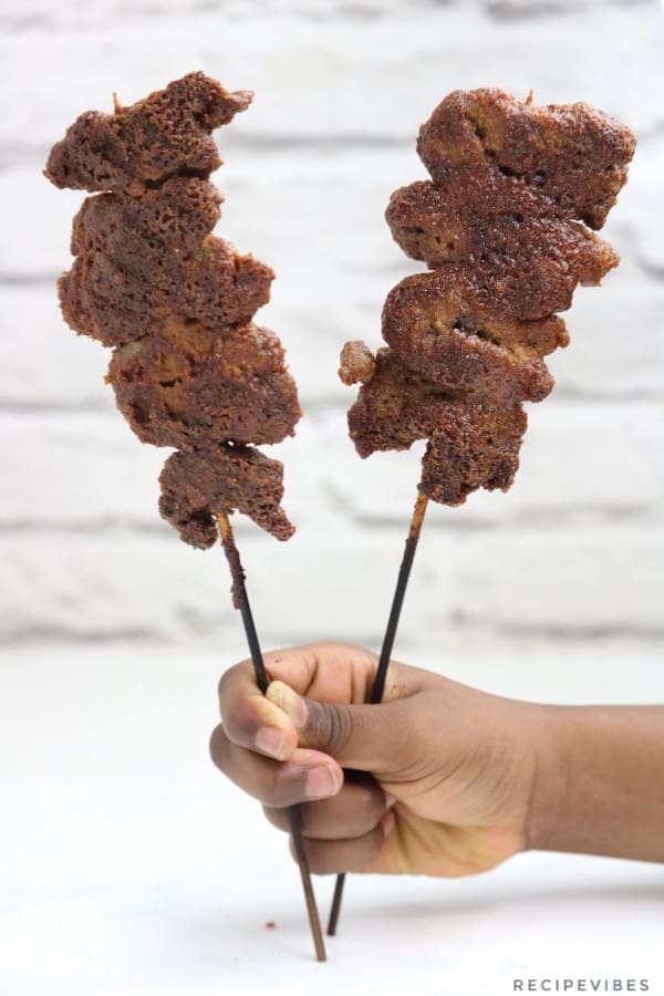 2 sticks of suya held up with one hand.