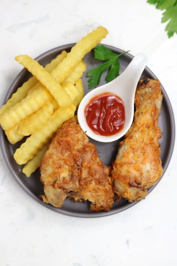 fried chicken served with fries and ketchup on a grey plate.