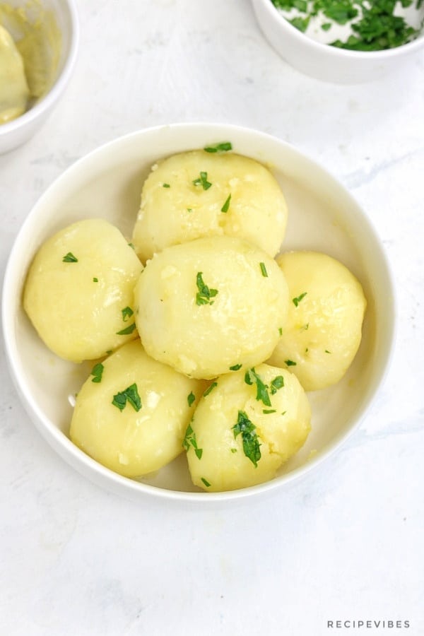 Boiled potatoes served in white plate and garnished with chopped parsley.