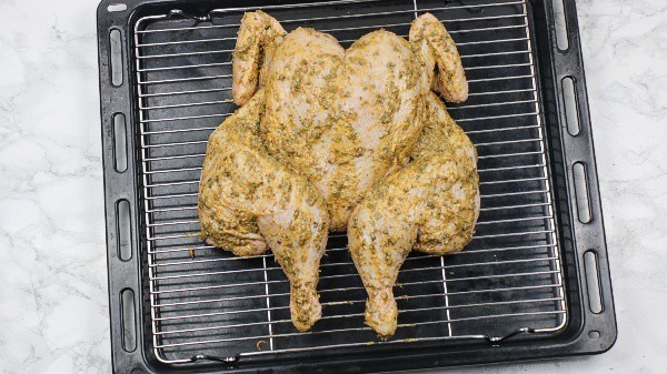The marinated chicken on oven rack over oven tray.