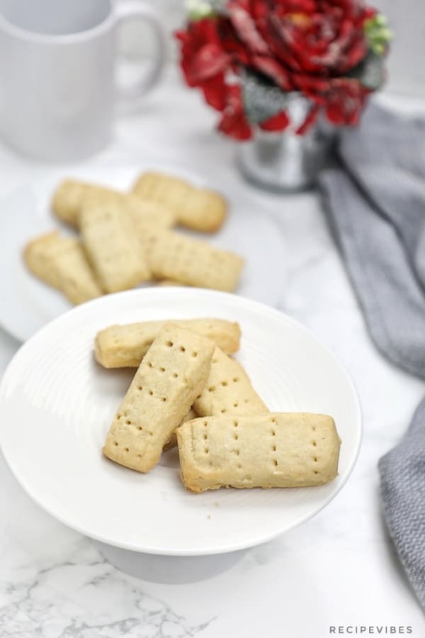 the shortbread cookies displayed on 2 white plates with grey napkin and red flower pot in background..