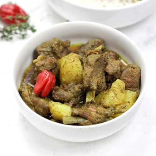 curry goat served in a white plate and garnished with whole scotchbonnet.