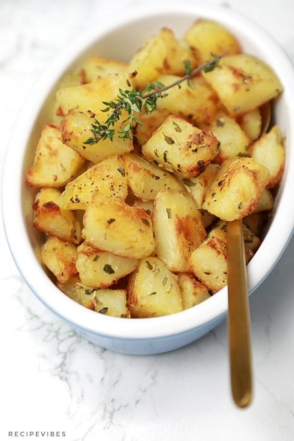 Roasted cubed potatoes served with a spoon for dishing in the plate.